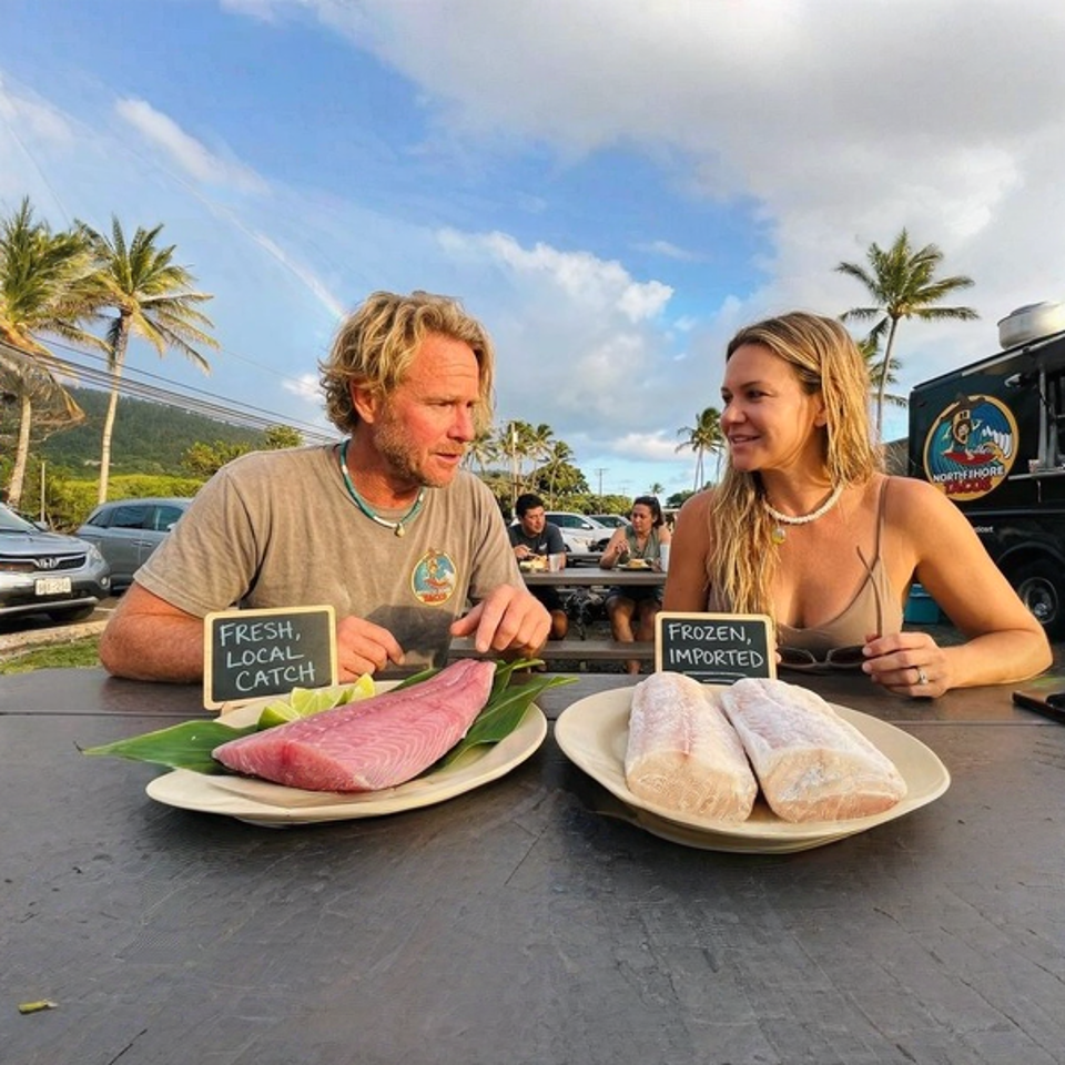 Two people at a picnic table with fresh tuna and frozen fish, a food truck in the background.